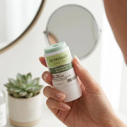 Hand holding a Dr. Melanin Cactus skincare product with a mirror and plant in the background